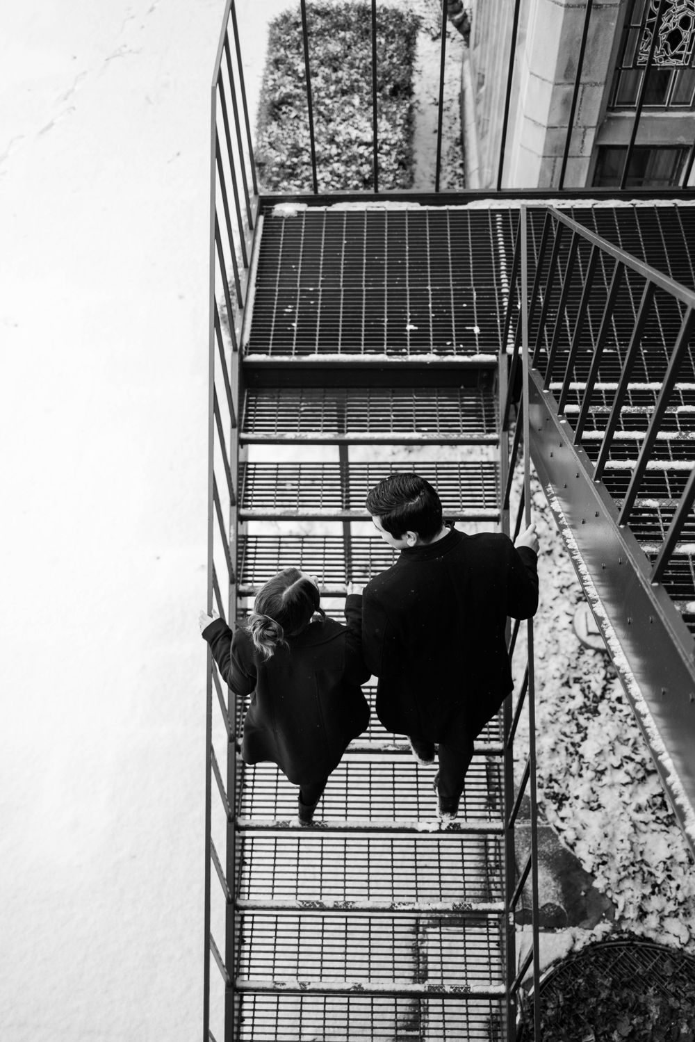 Couple descends metal stairs together in dramatic black and white composition.