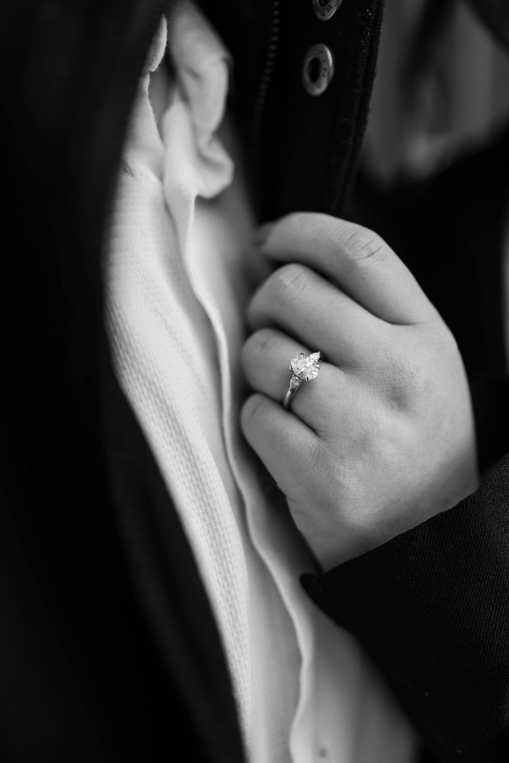 Close-up of an engagement ring on a hand against dark fabric.