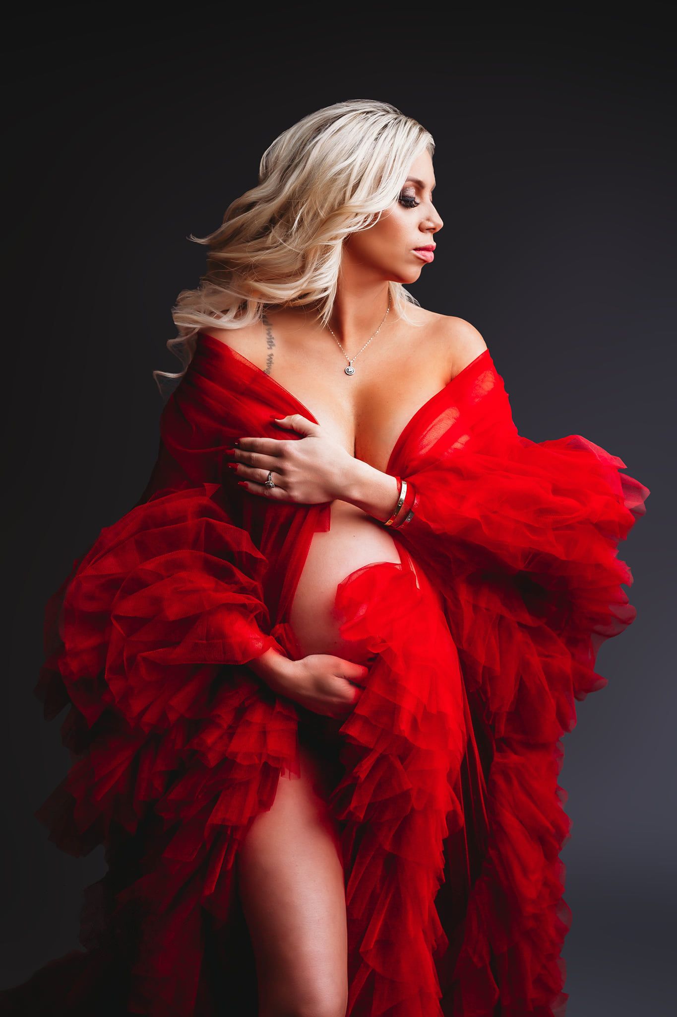 Dramatic portrait featuring red tulle gown against dark studio background.