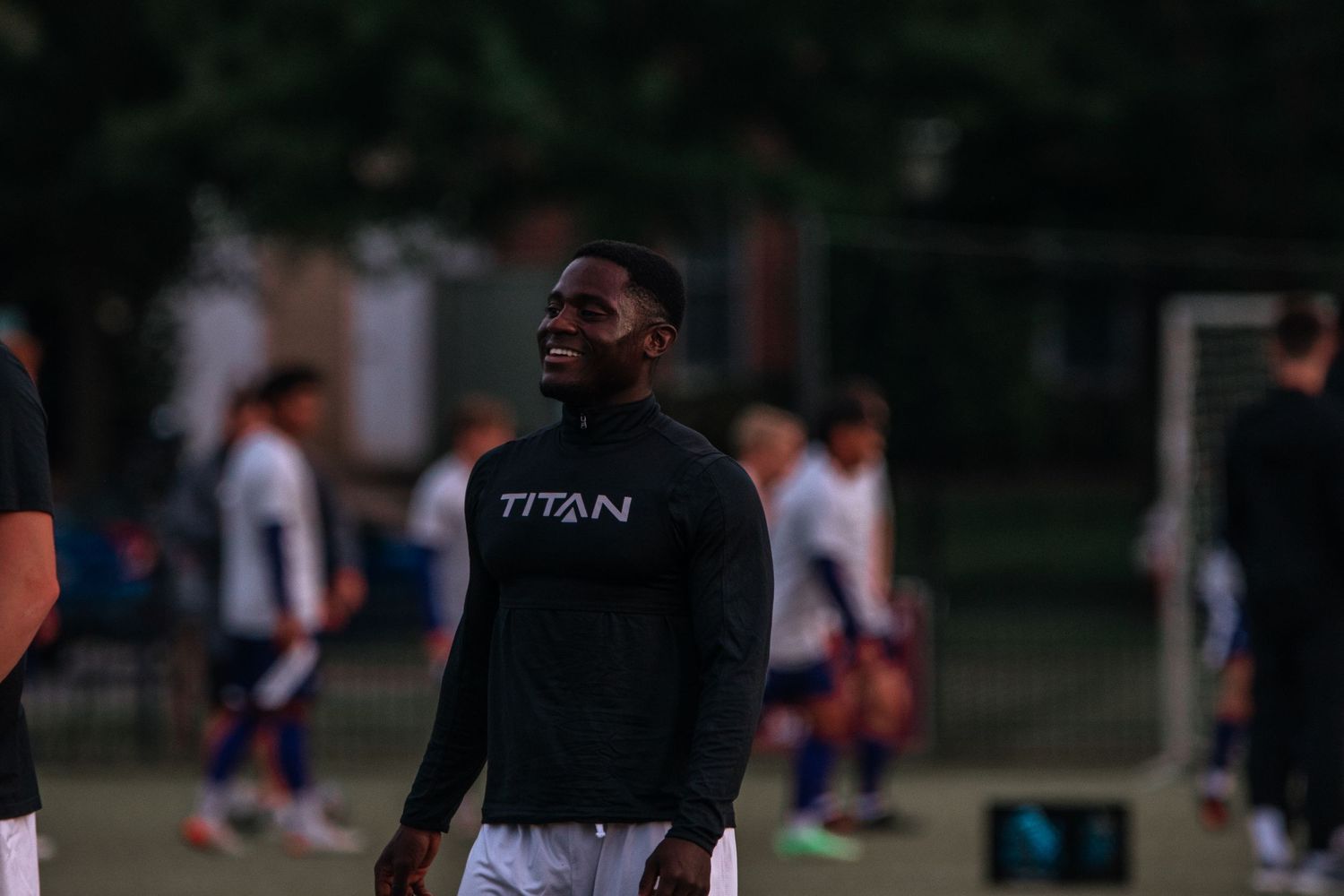 Athlete in a black Titan sweatshirt stands on a sports field during practice or training session.
