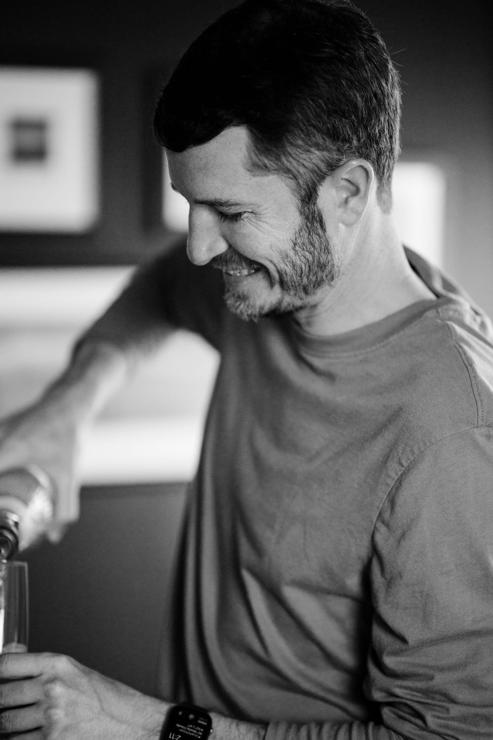 Person in casual attire smiling while opening a bottle.