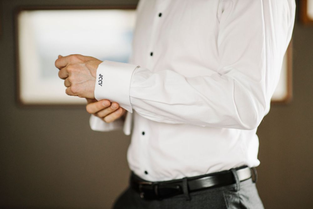 Close-up of someone adjusting the sleeve cuff on a crisp white dress shirt.
