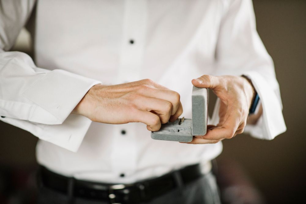 Hands holding and opening a small gray ring box.