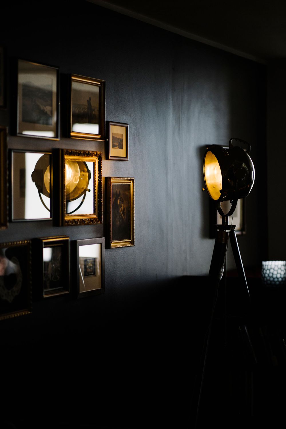 Vintage spotlight lamps illuminate a dark room with framed artwork on the wall.