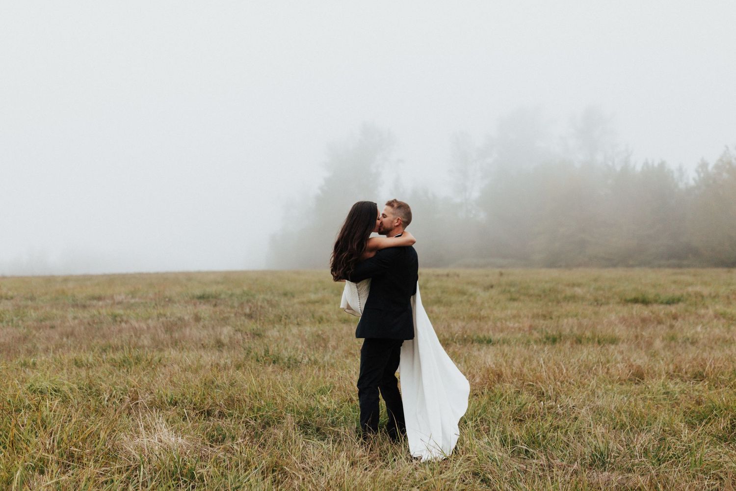 Couple embraces in a misty field creating a romantic silhouette against the foggy landscape.