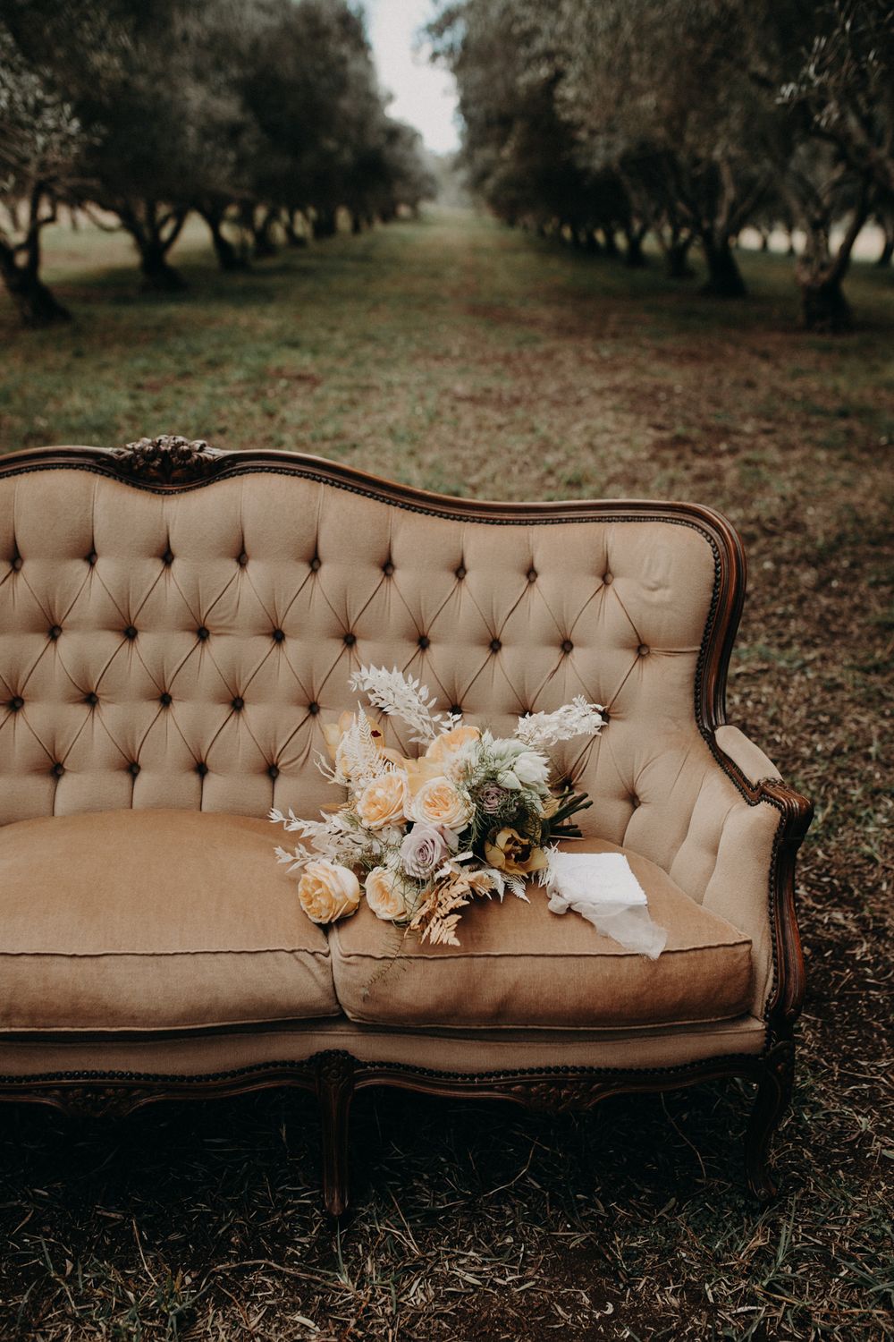 Vintage tufted sofa with floral bouquet in an orchard setting.