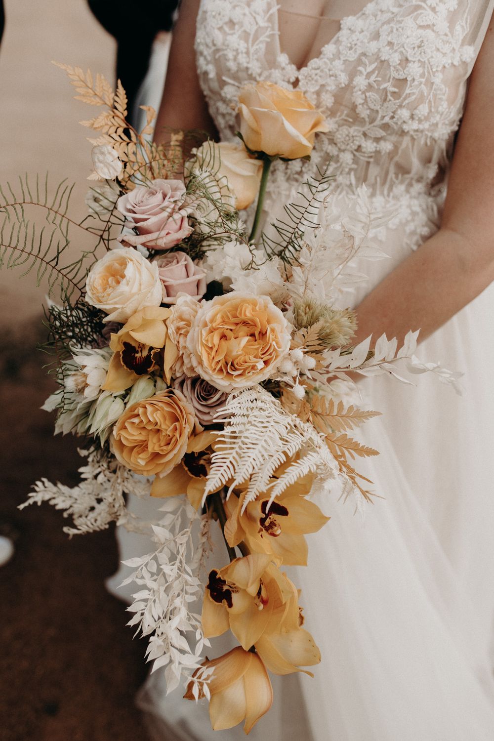 Elegant bridal bouquet featuring peach and cream roses with dried ferns and delicate foliage.