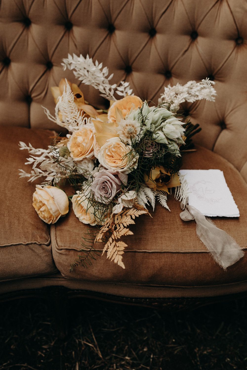 Elegant wedding bouquet with peach roses and white flowers on brown tufted leather couch.