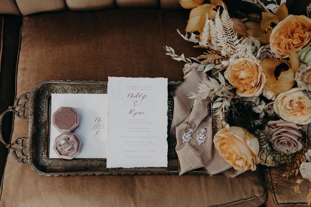 Wedding invitation and vintage tray styled with peach roses on brown leather sofa.