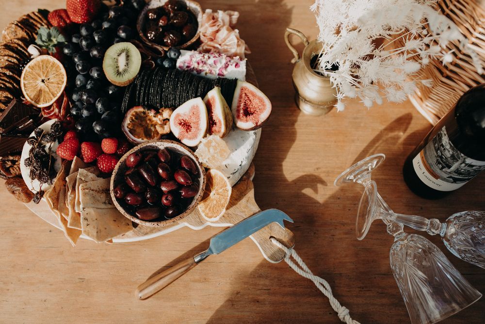 Rustic table setting with fresh fruits, figs, and grapes arranged on wooden surface with glassware.