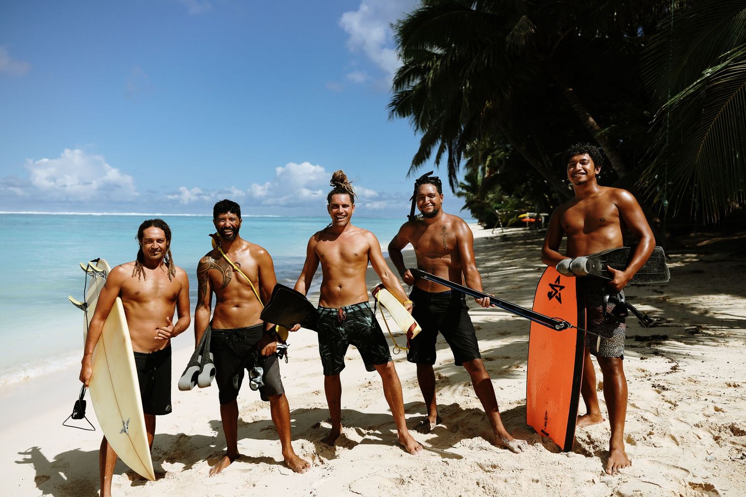 Group of surfers with surfboards standing on a tropical beach with palm trees.