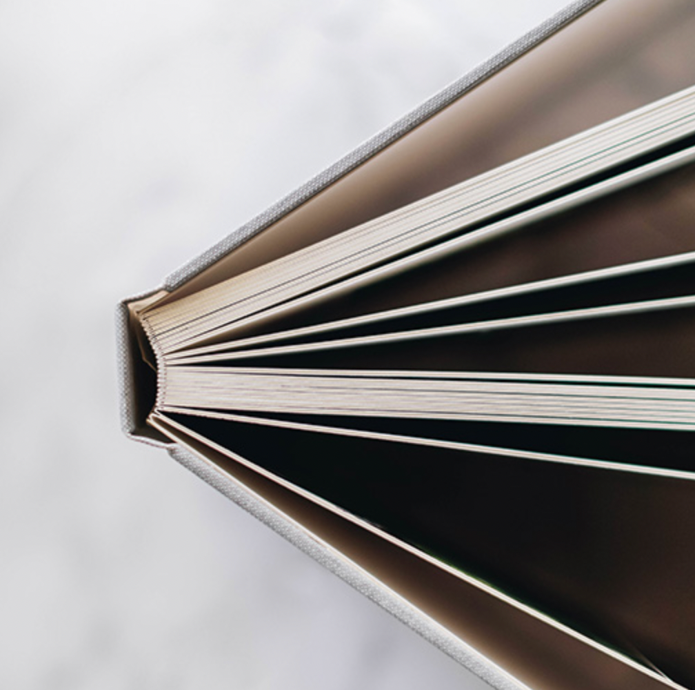 Close-up top view of an open hardcover book with fanned pages on marble surface.
