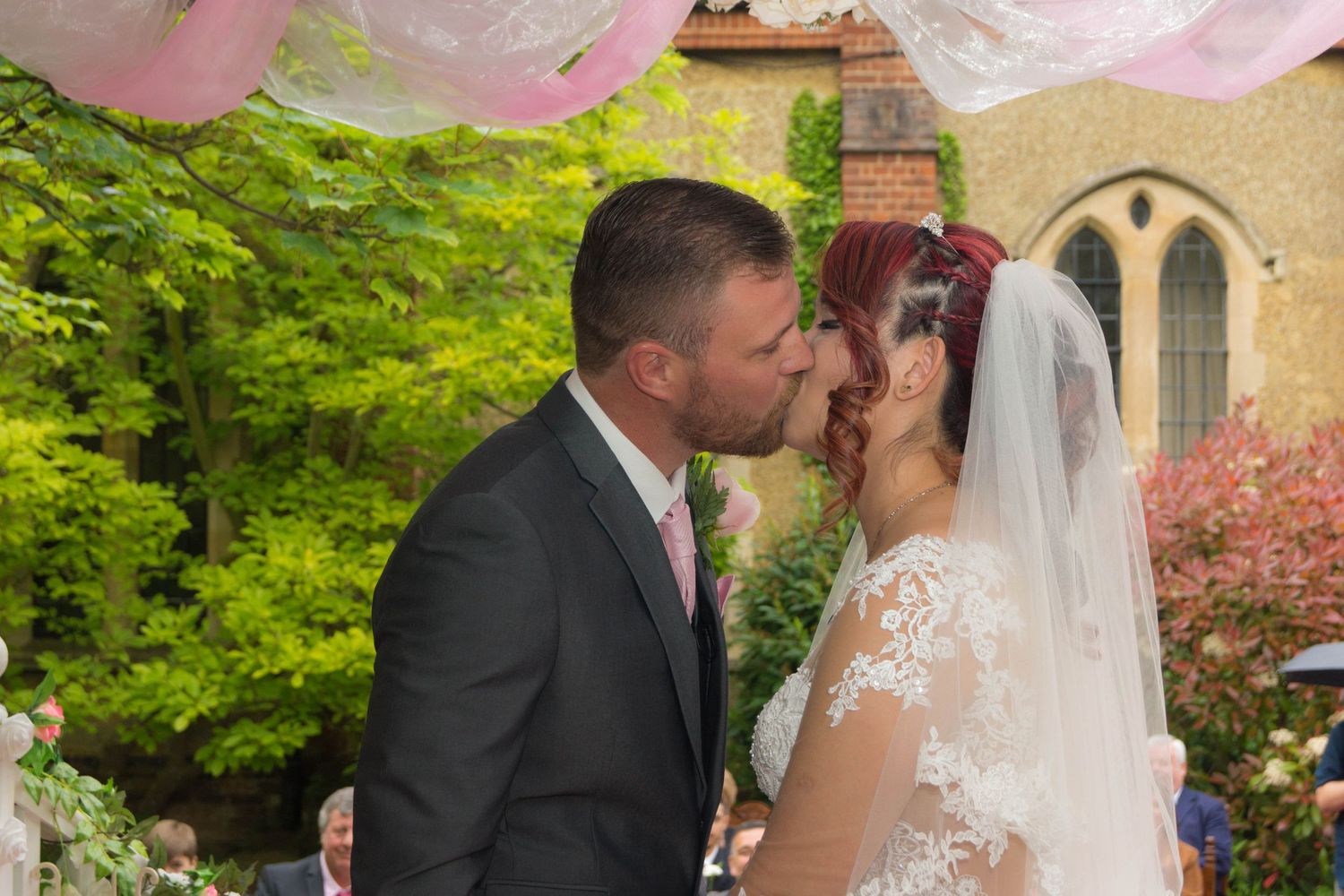 A tender wedding kiss moment captured in front of a church with pink spring blossoms.