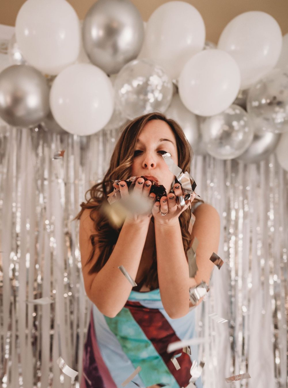 Festive party photo blowing confetti with silver and white balloon decor.