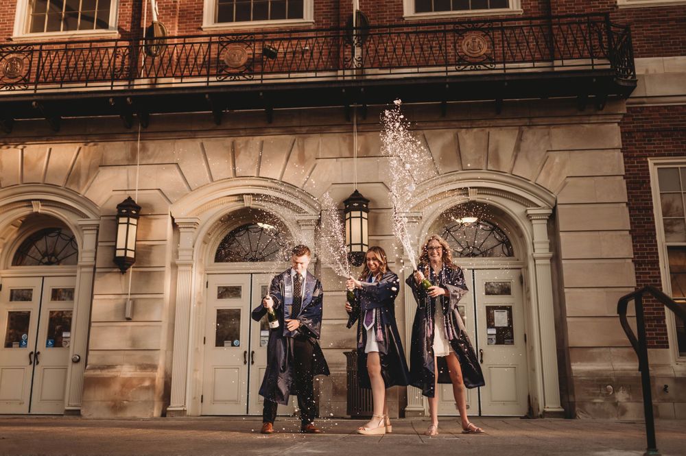 Group celebration with champagne spray in front of historic building entrance.