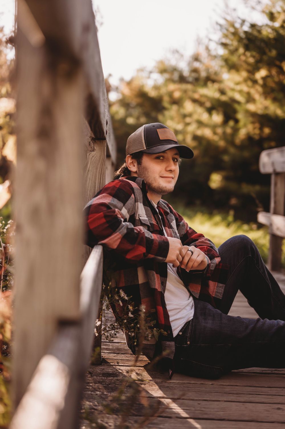 Person in flannel and cap relaxing on wooden deck in autumn sunlight.