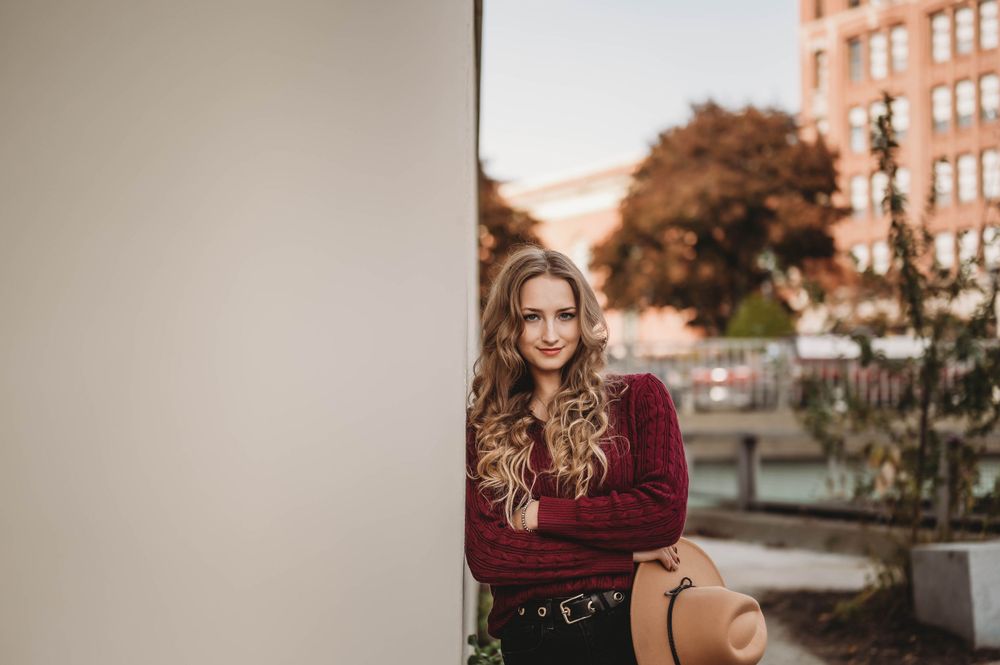 Artistic urban portrait with burgundy sweater against white wall in autumn setting.