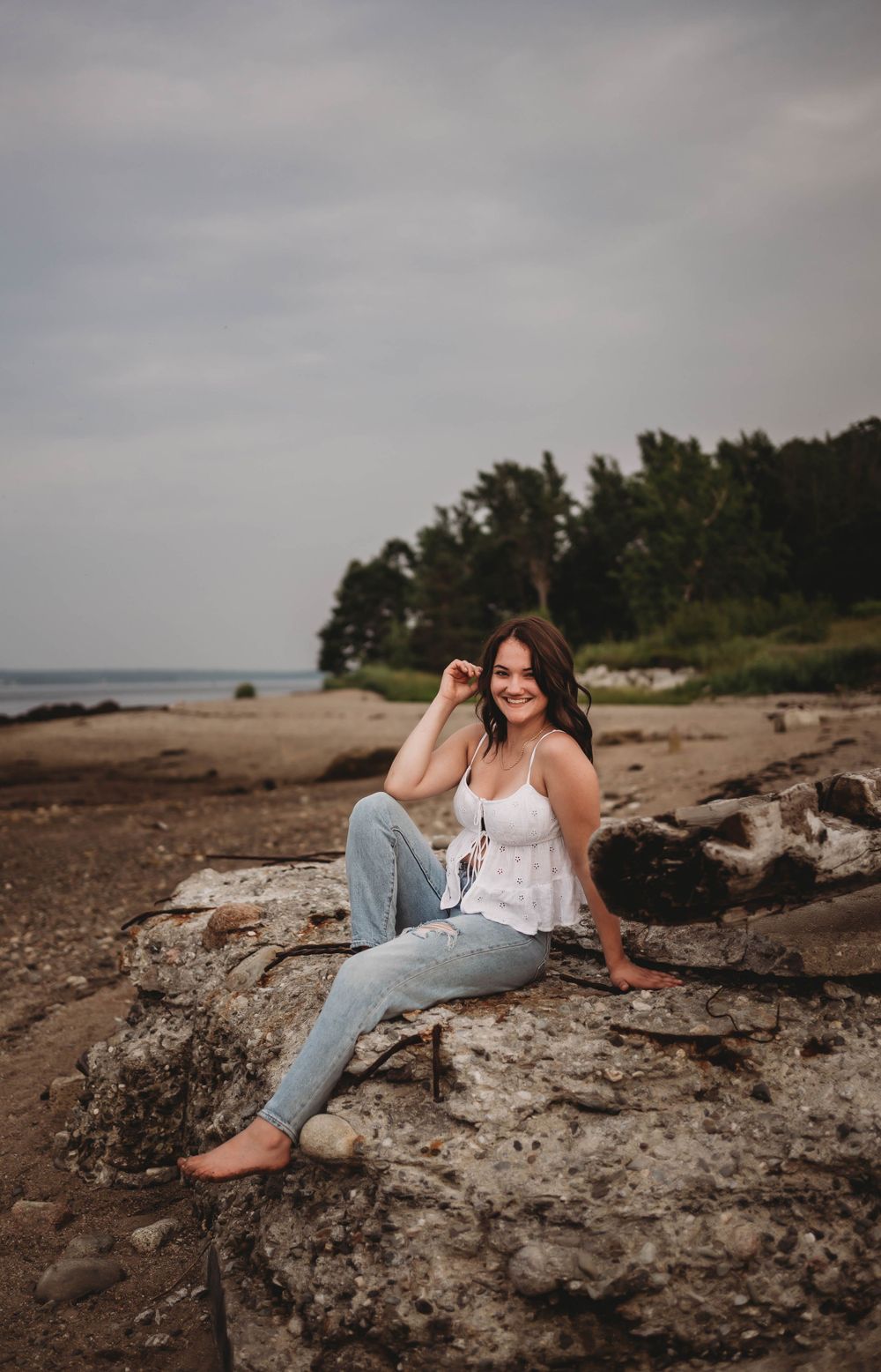 Casual portrait on coastal rocks with ocean and trees in the background.