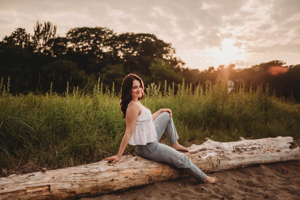 A sunset photoshoot on a fallen log amidst tall grass showcases casual summer style with white top and jeans.