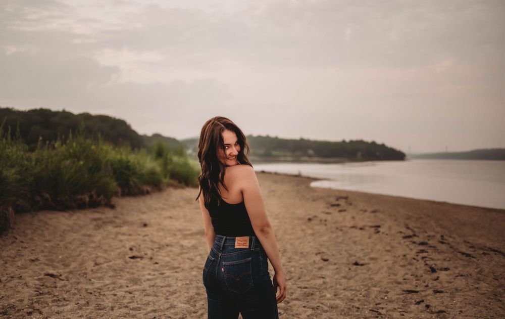Sunset beach portrait features casual style with denim against water backdrop.