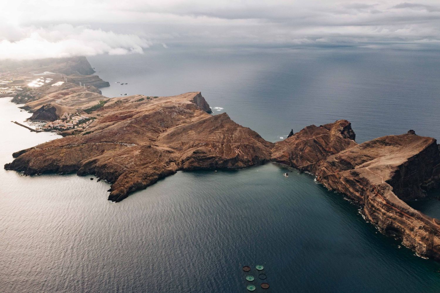 Aerial view of dramatic coastal cliffs and rugged headland jutting into dark blue ocean waters.