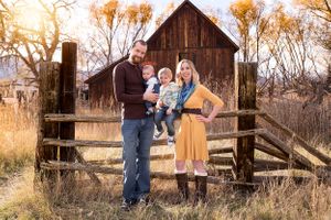 Family standing by rustic barn and wooden fence during golden hour.