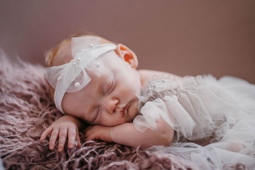 Sleeping newborn baby wearing white lace on pink textured blanket.
