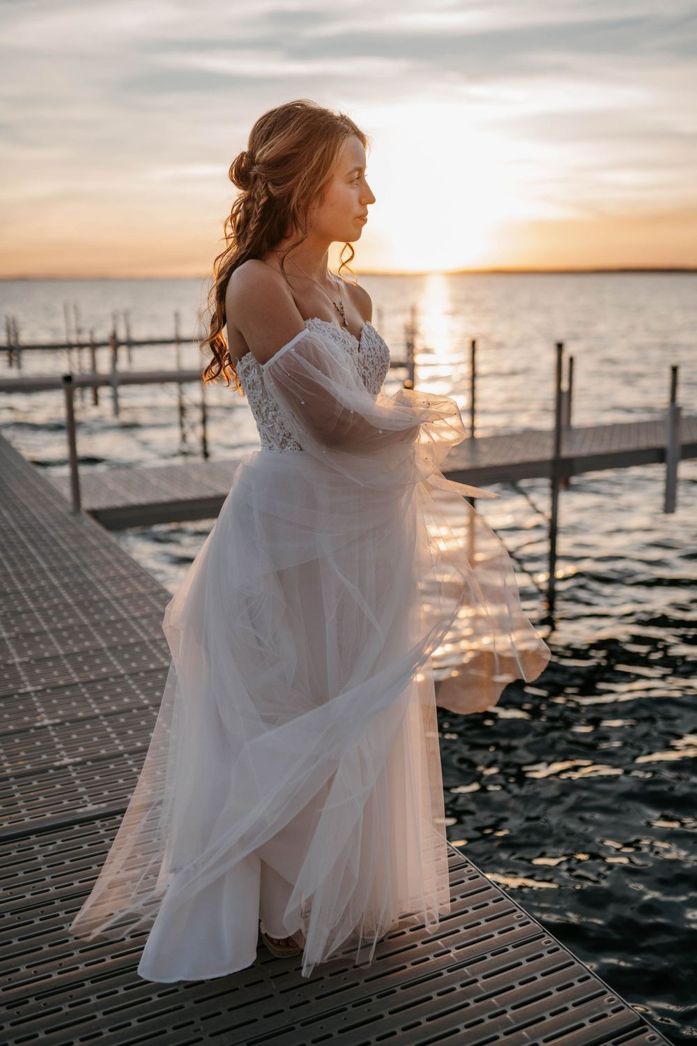 Ethereal sunset photoshoot on a dock with flowing white dress and golden light reflecting on water.