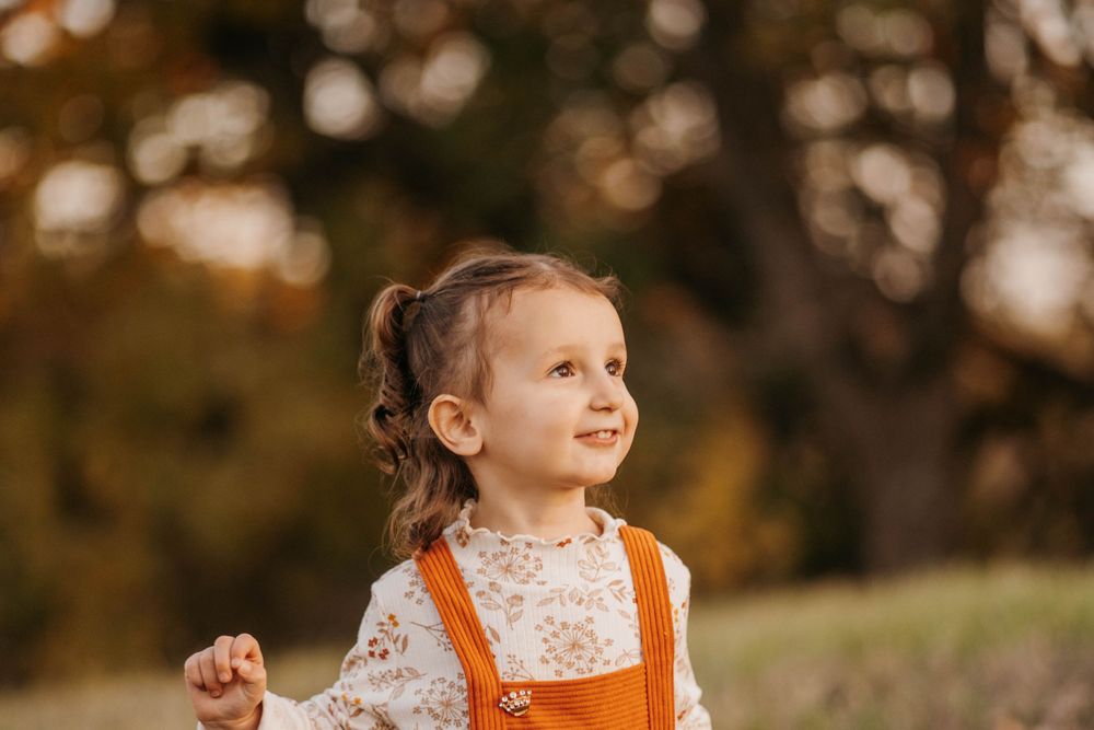 Child in orange dress playing outdoors during golden sunset.