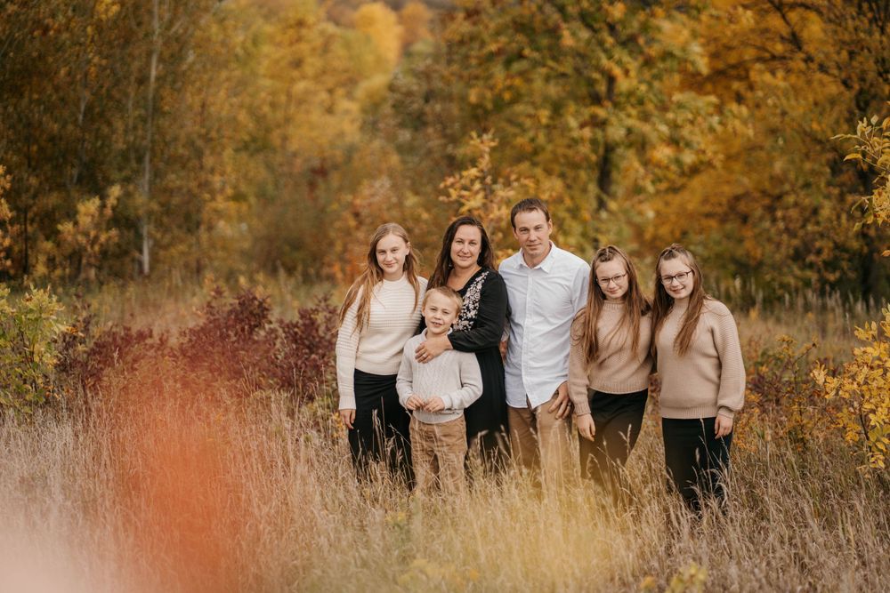 Family portrait session in a field with golden autumn foliage and warm afternoon light.