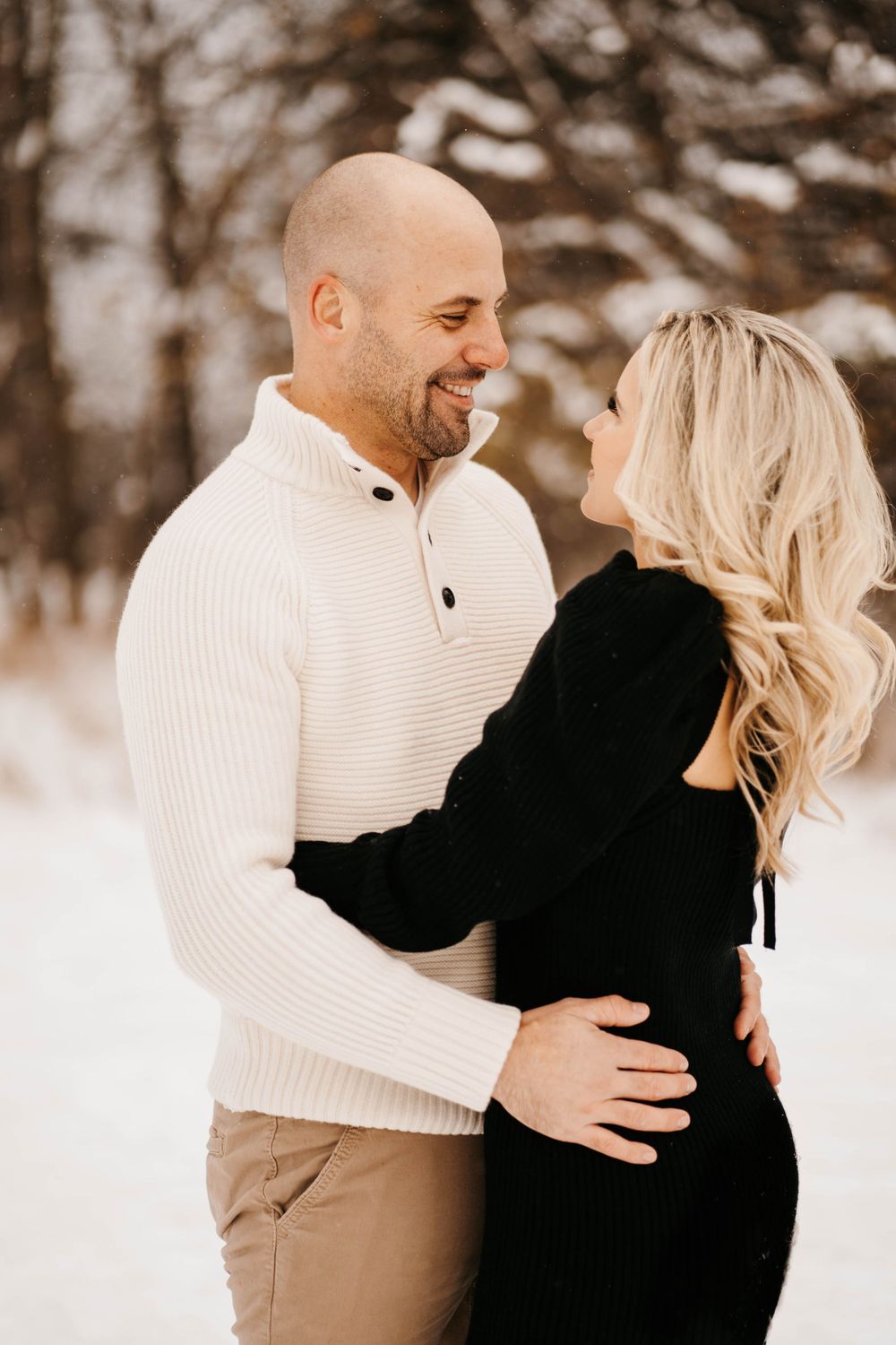 Couple in winter clothing embracing and laughing in snowy setting.