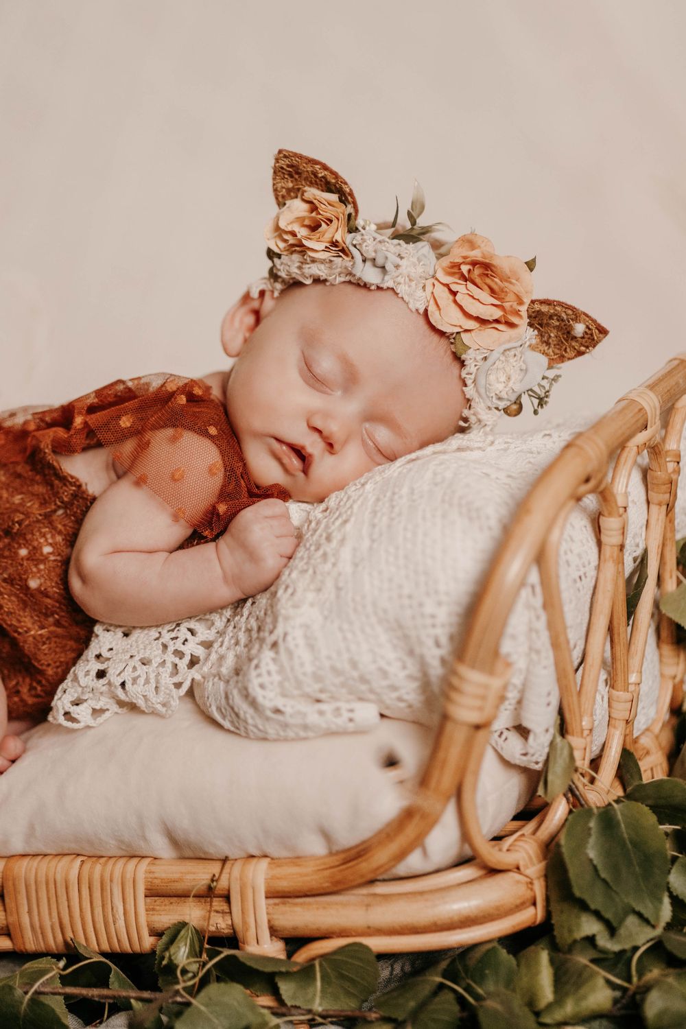 Newborn baby sleeping peacefully in vintage wooden basket with floral accents.