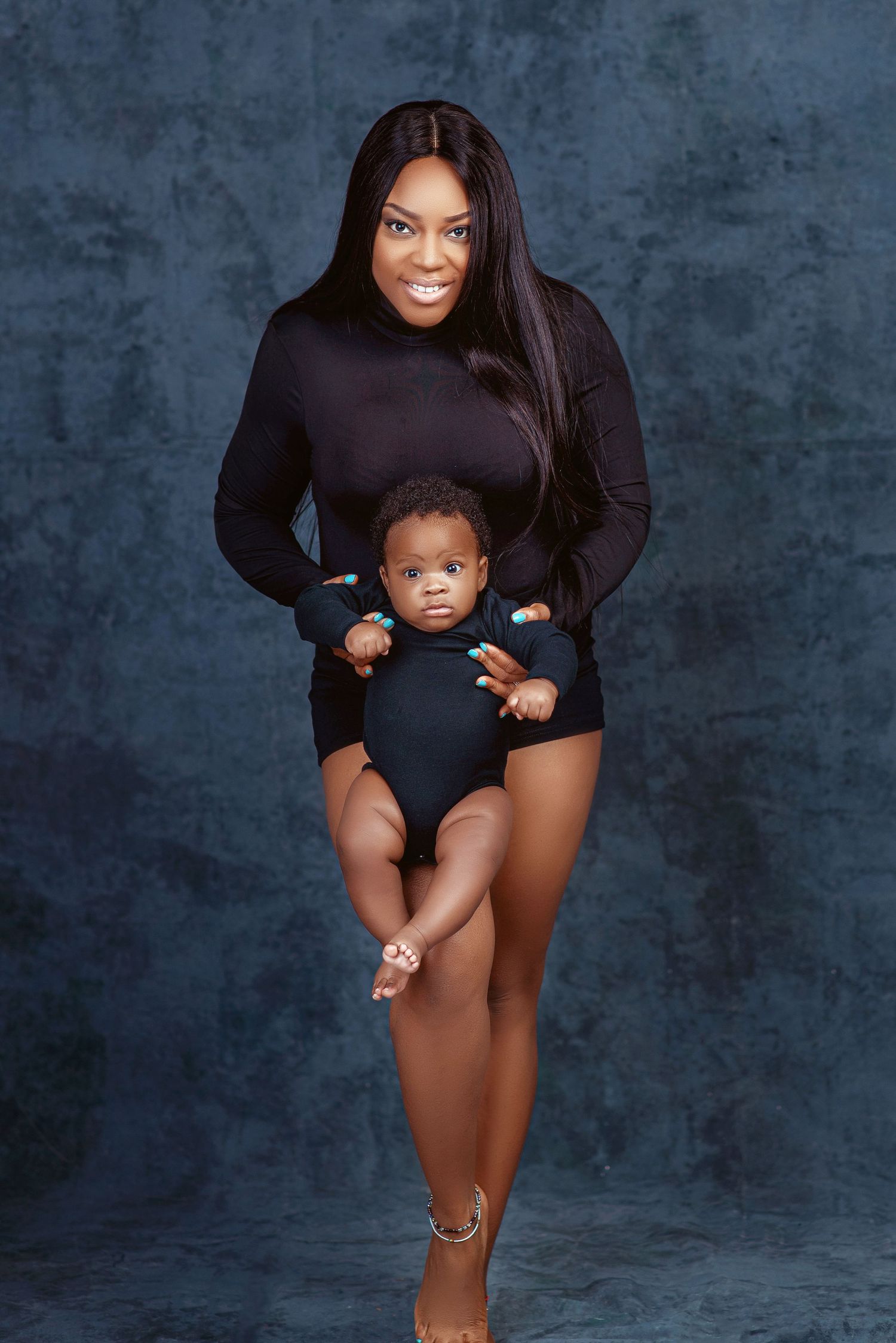 Studio portrait session with matching black outfits against blue textured backdrop.