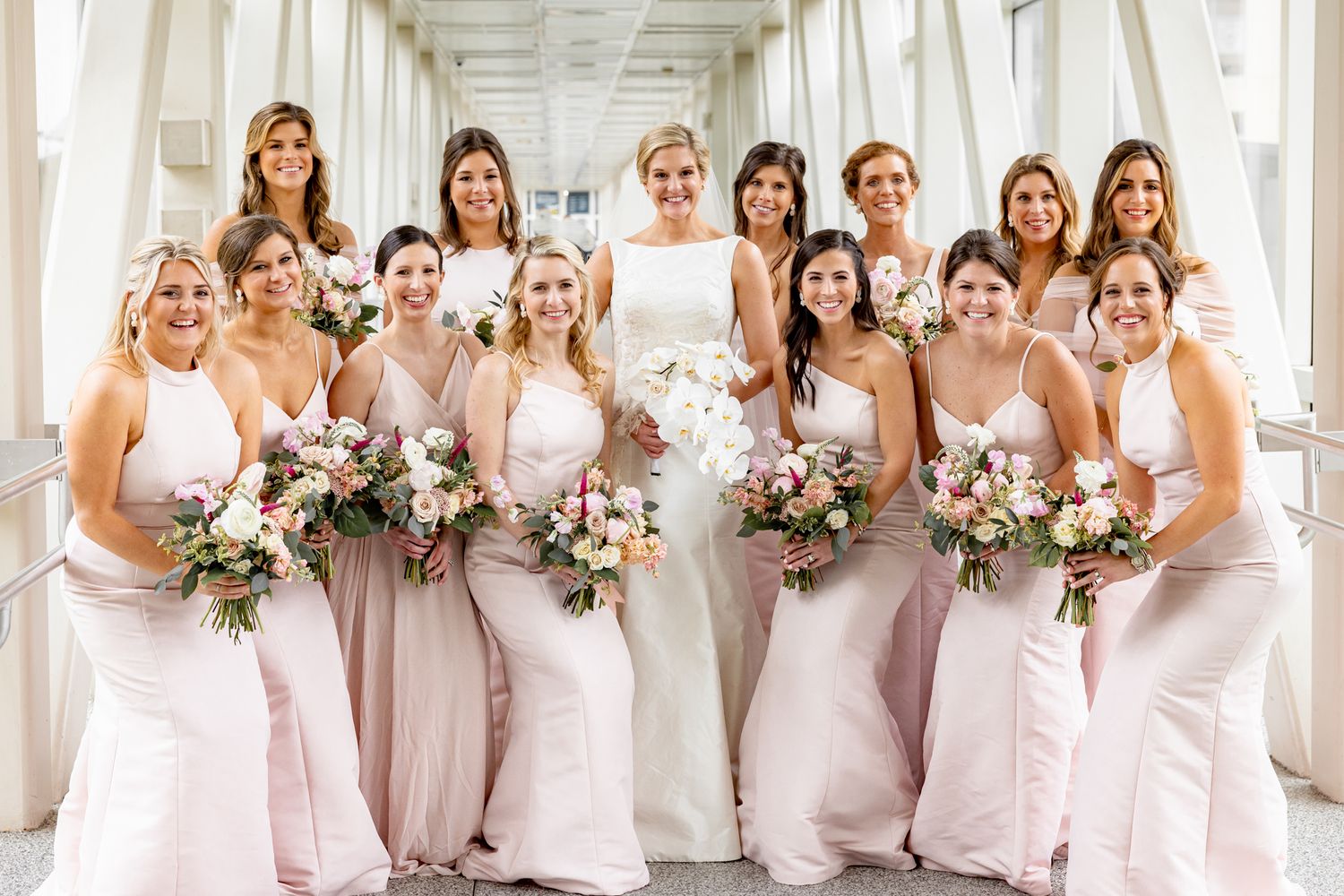 Bride and bridesmaids posing in a walkway, holding bouquets and looking stunning in a group photo.