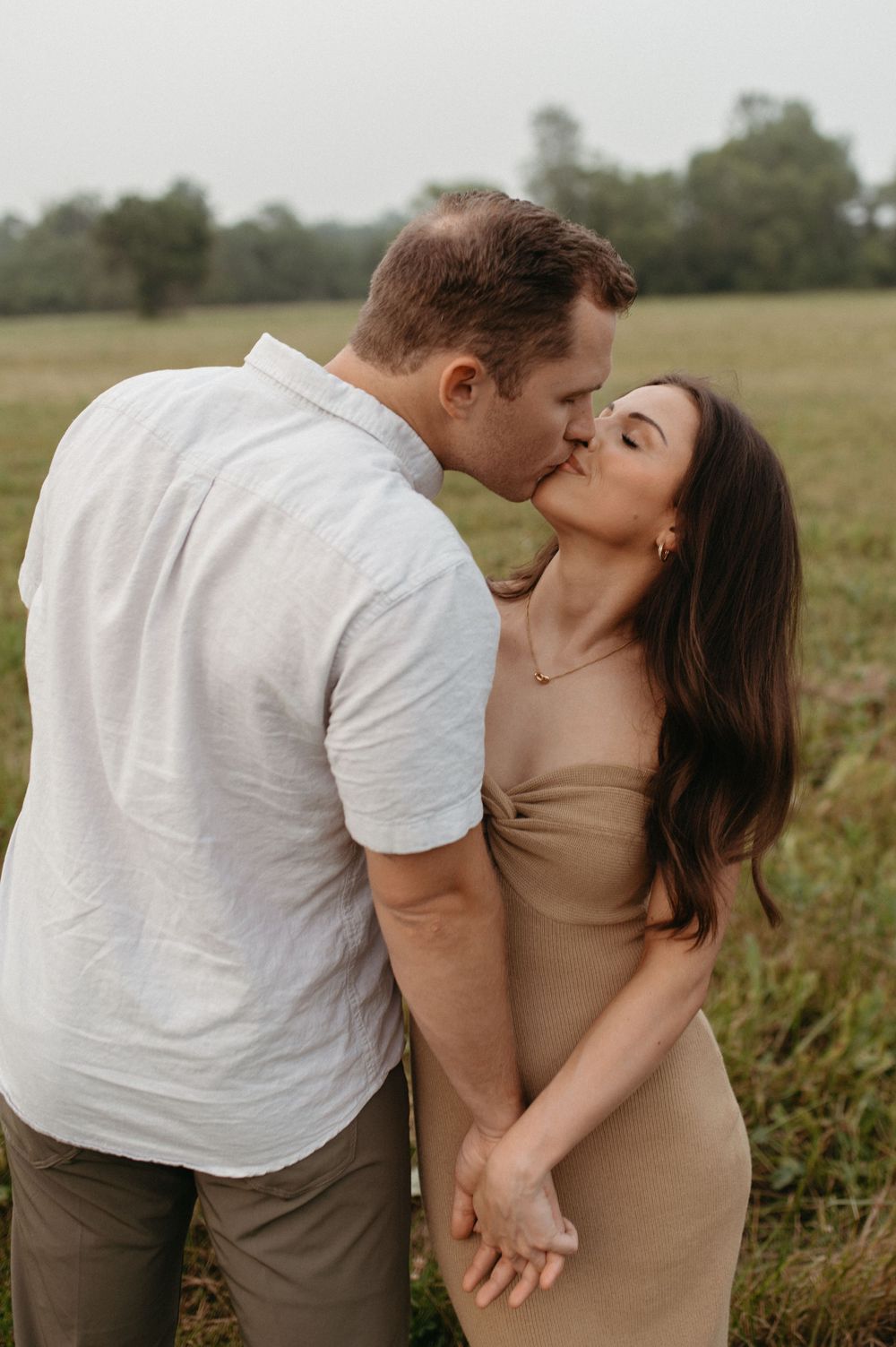 A romantic kiss shared between a couple in a field wearing casual summer attire.