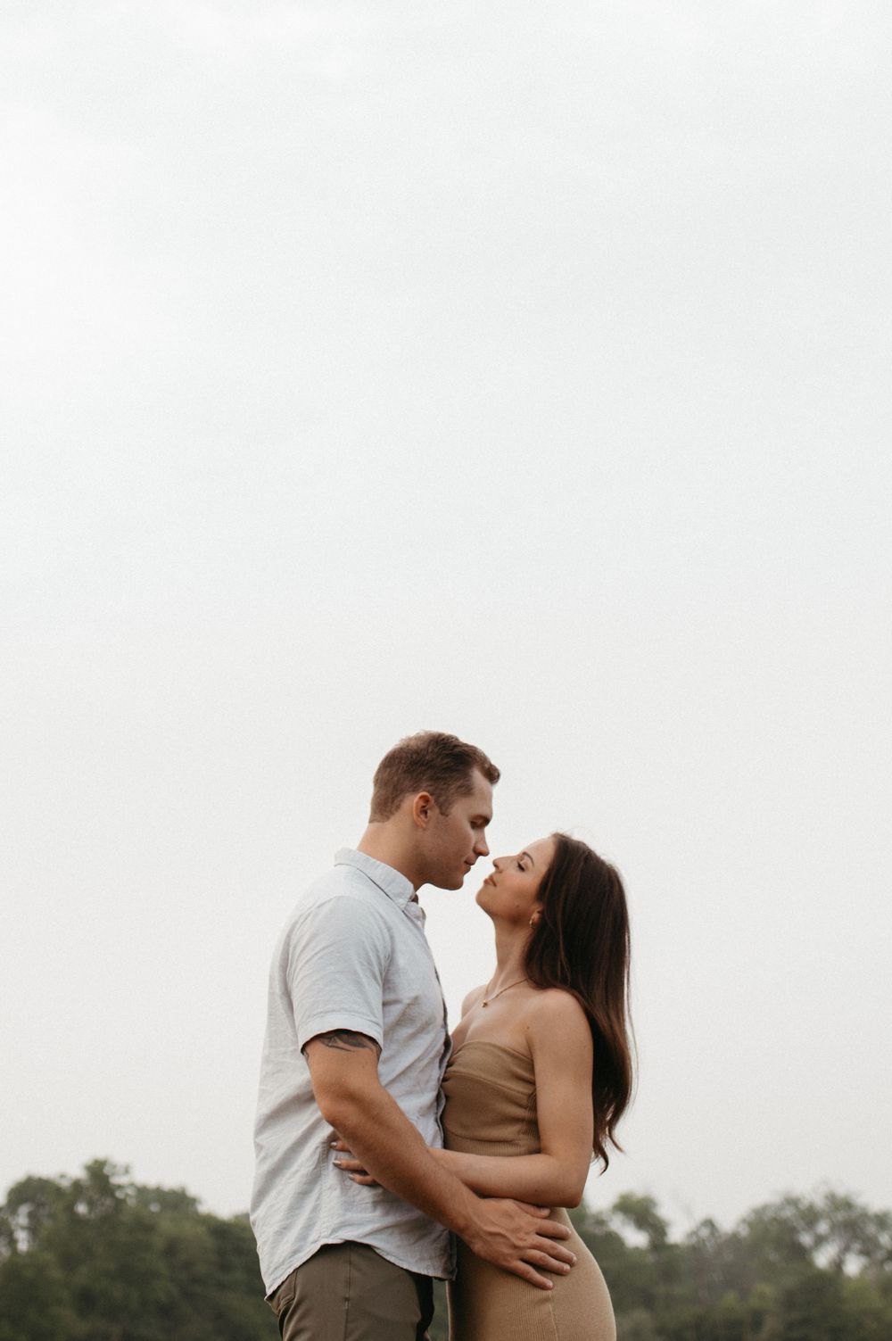 A romantic couple in coordinated outfits embrace tenderly against an overcast sky.