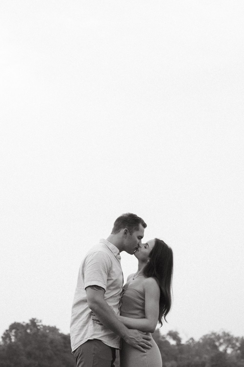 A romantic black and white portrait of a couple embracing in a field.