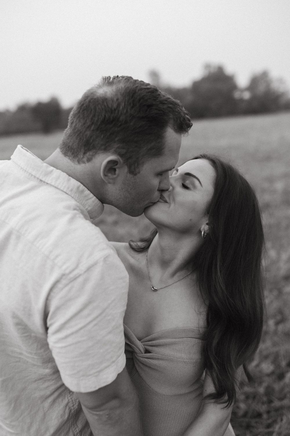 Black and white portrait of a tender kiss between a couple in an outdoor setting.