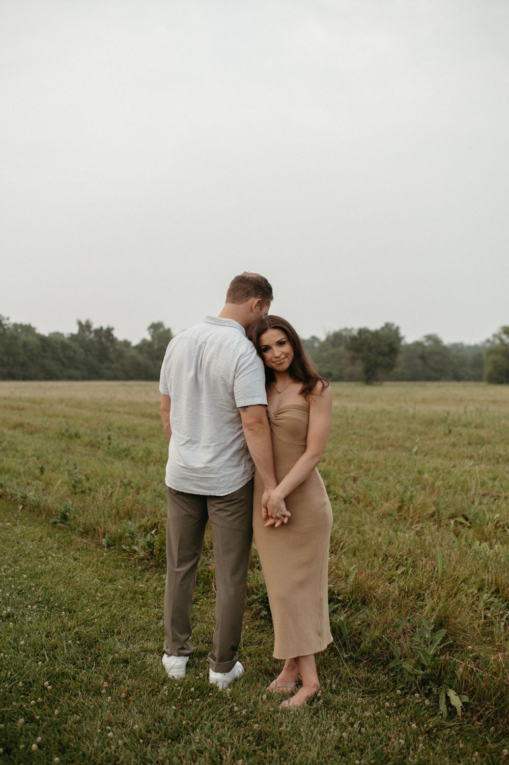 A tender moment between a couple holding hands in a grassy field at dusk.