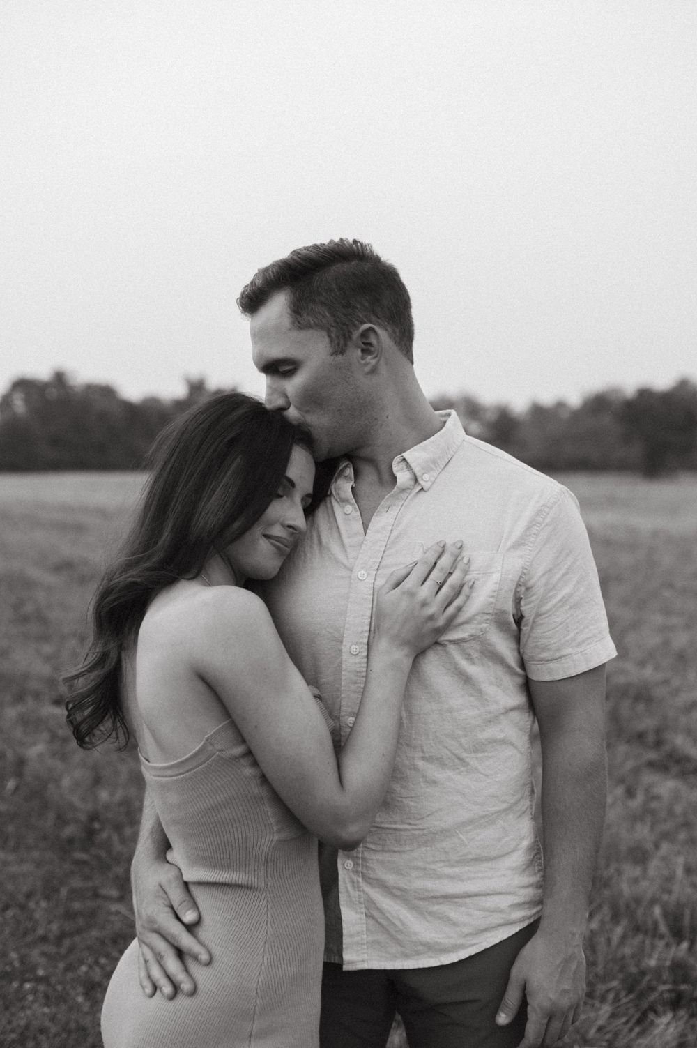 A romantic black and white photo of a couple embracing in a field, showing tender intimacy.