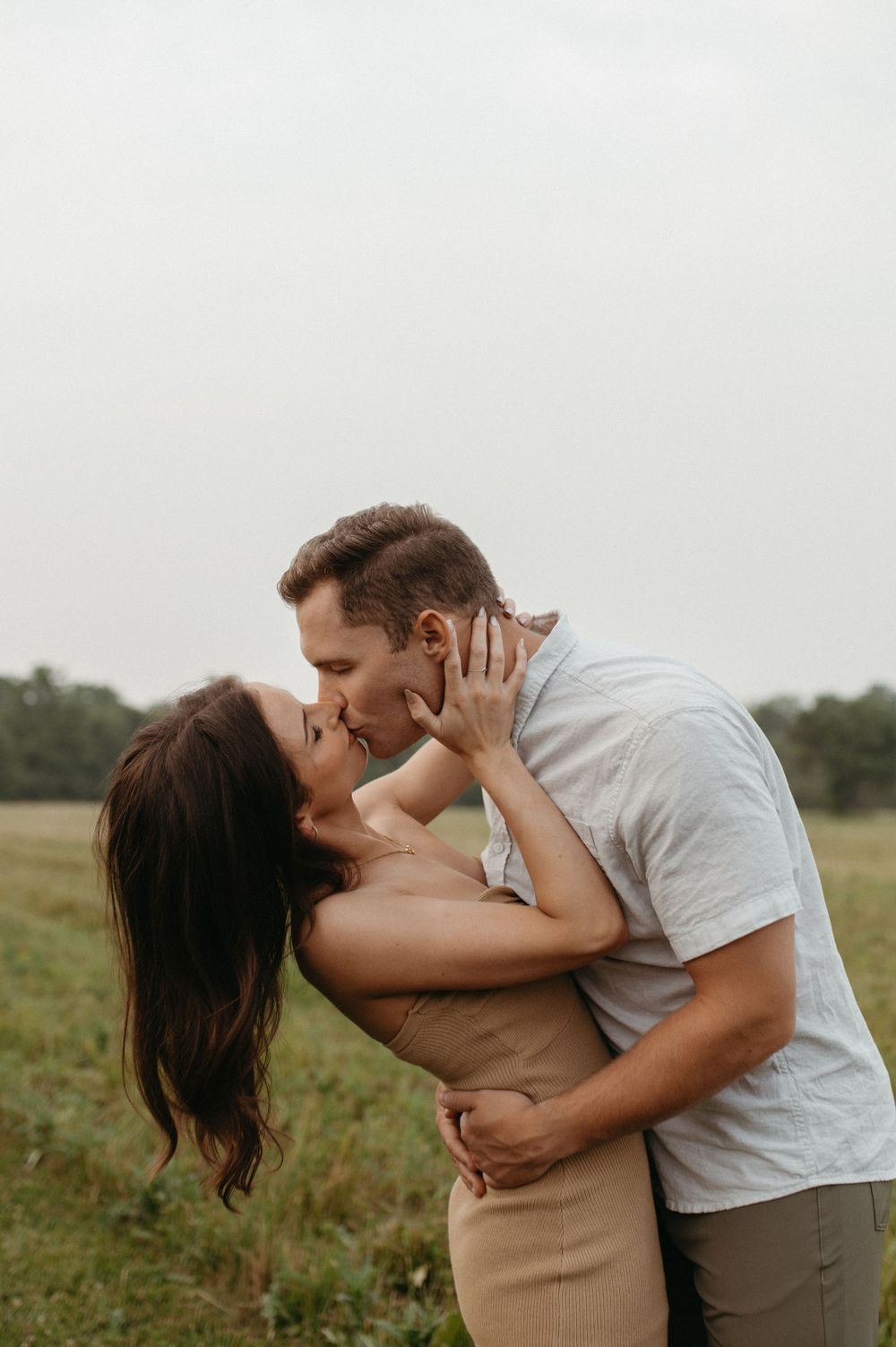 A passionate kiss shared between a couple in casual attire standing in a meadow.