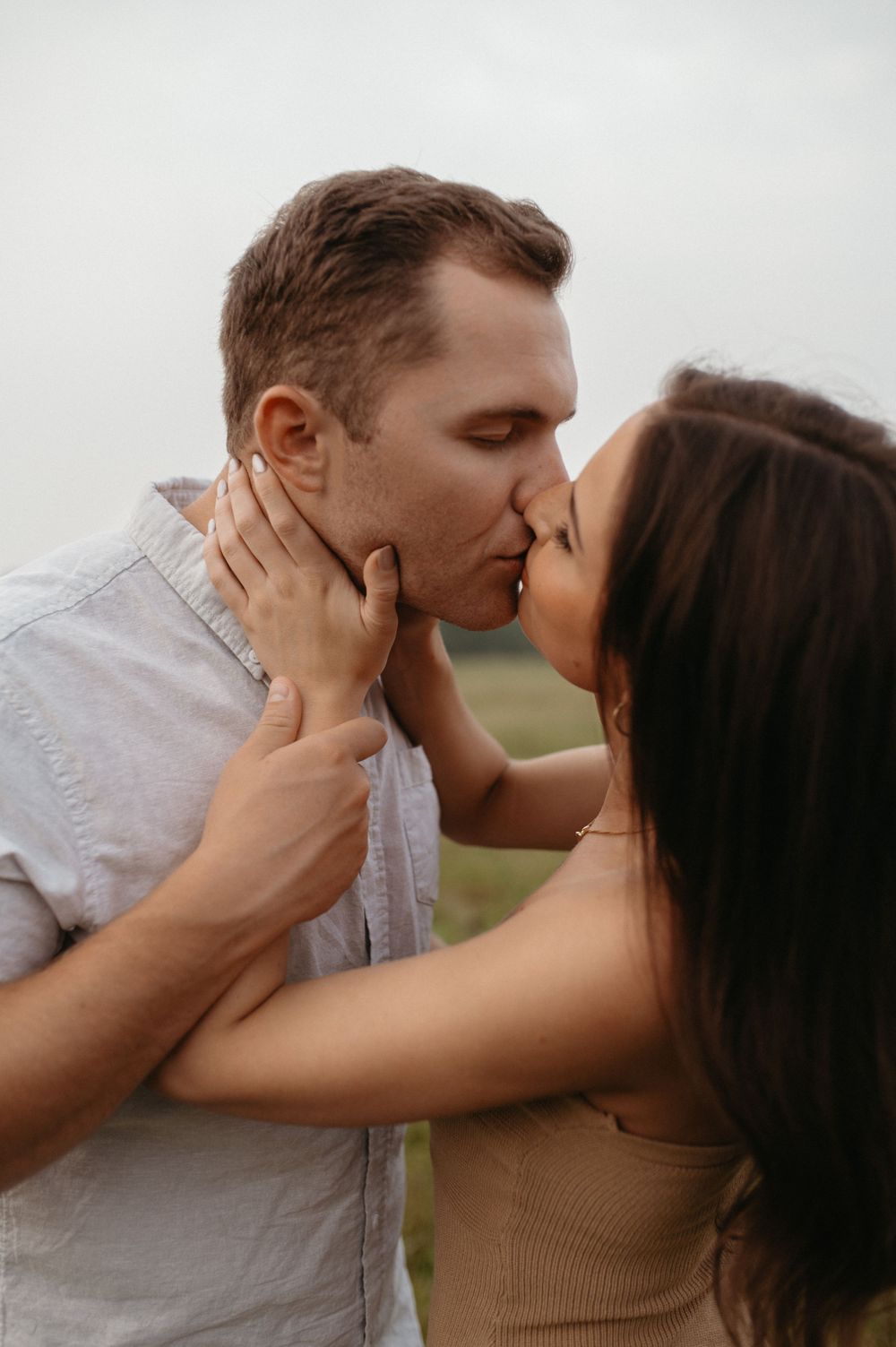 A romantic couple shares a tender kiss in a soft, intimate outdoor portrait.