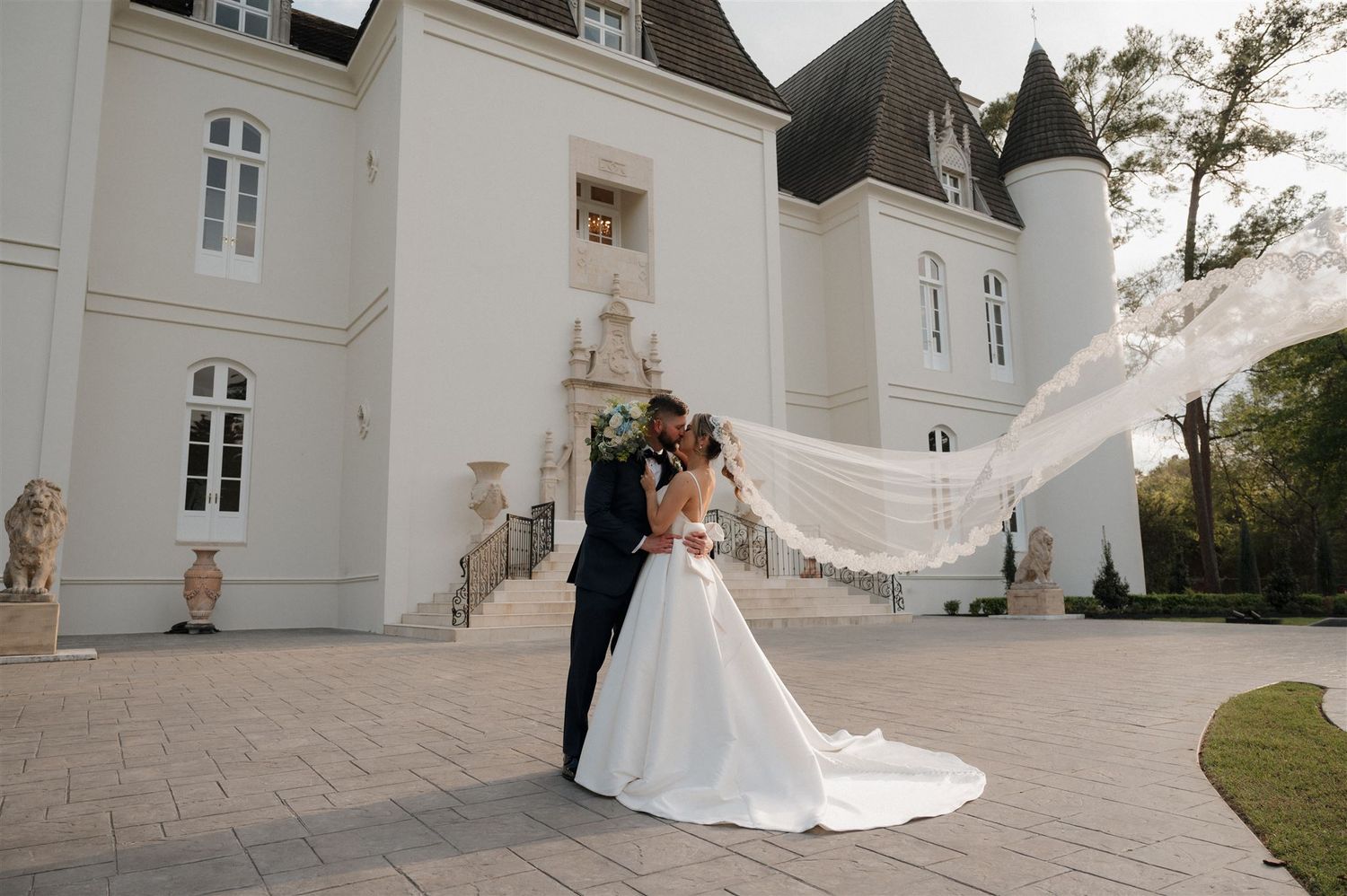 Elegant wedding photo at a white chateau with a flowing veil against the ornate castle architecture.