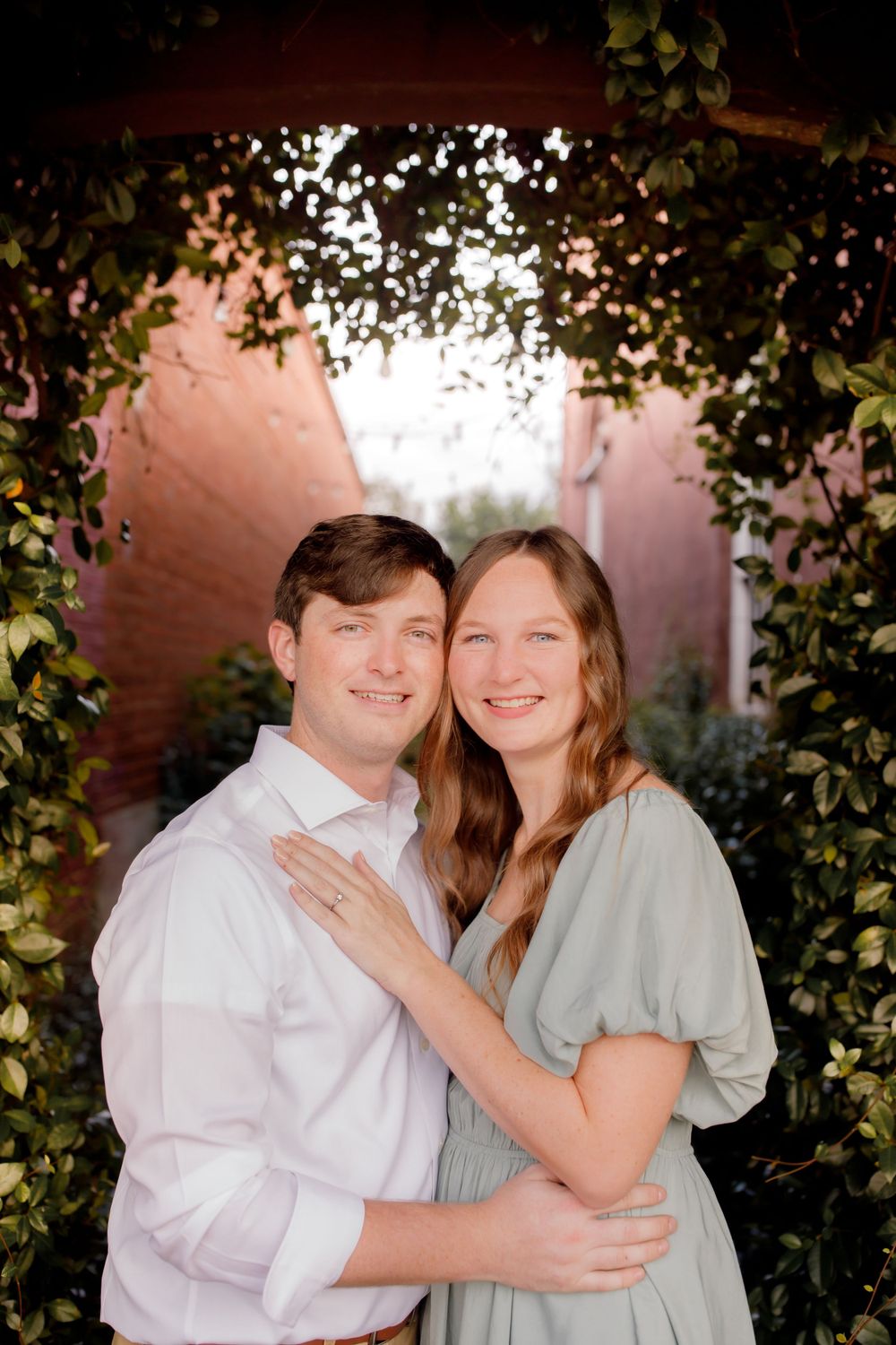 A romantic portrait of a couple smiling and embracing under a lush garden archway.
