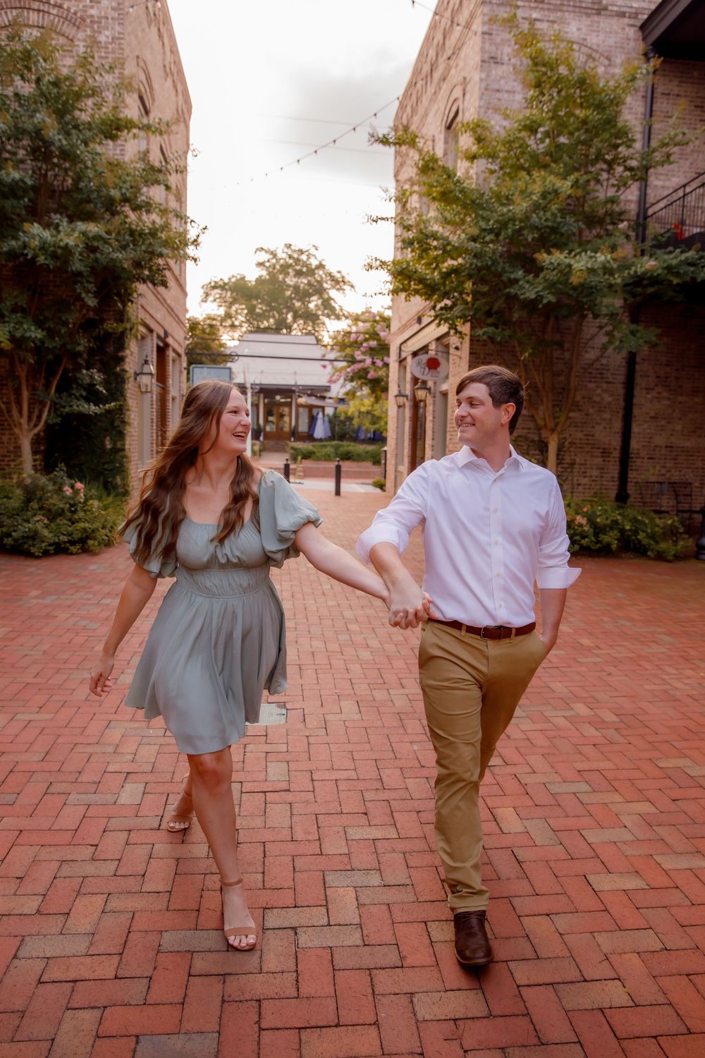 A couple walks hand in hand down a brick courtyard between historic buildings.