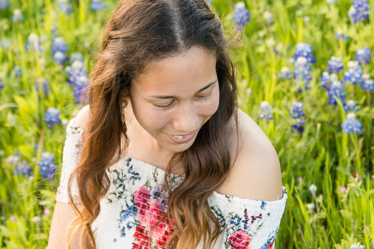 Woman in floral dress sitting amongst blooming blue wildflowers.