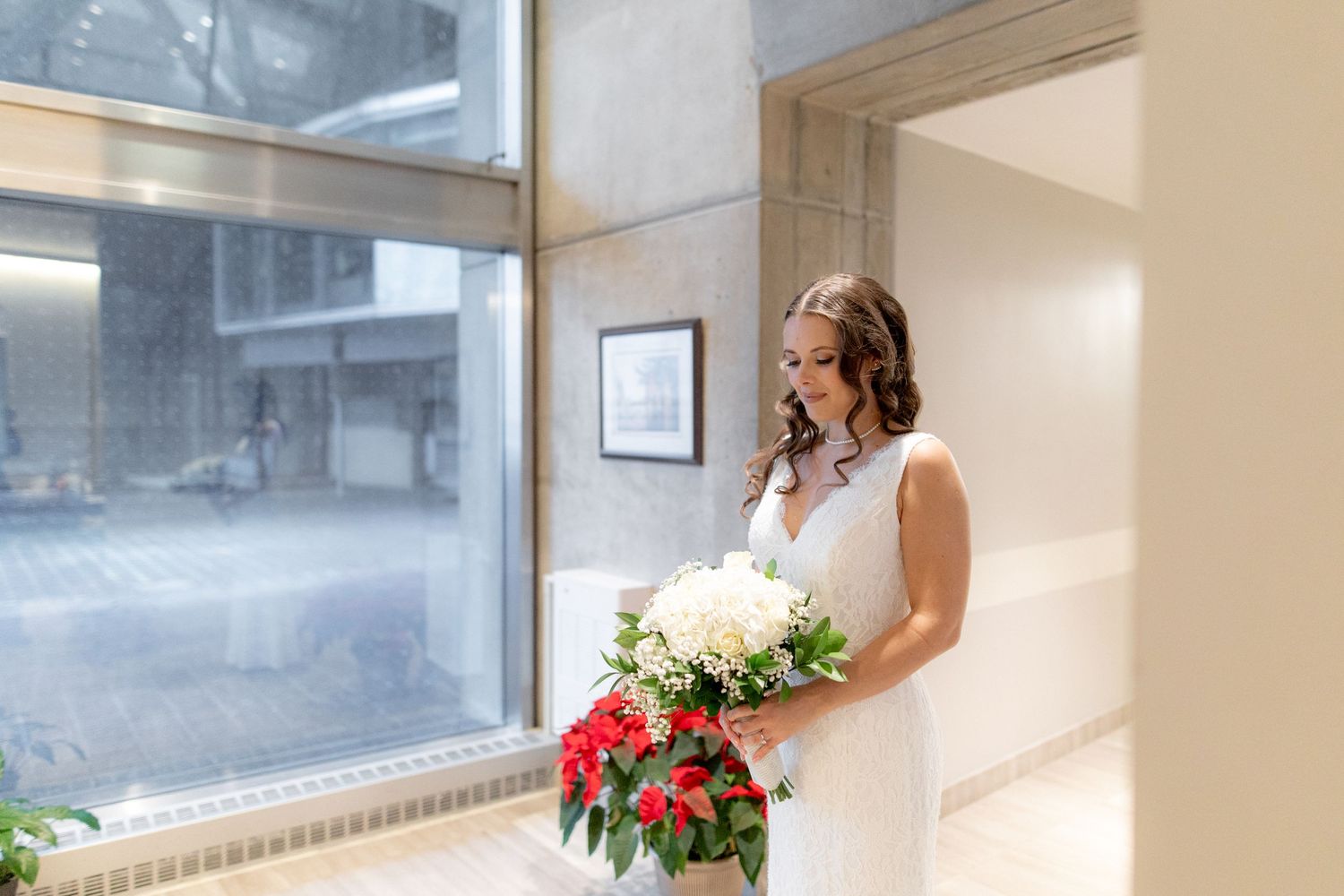 A bride holds a beautiful red and white bouquet while standing by a window.