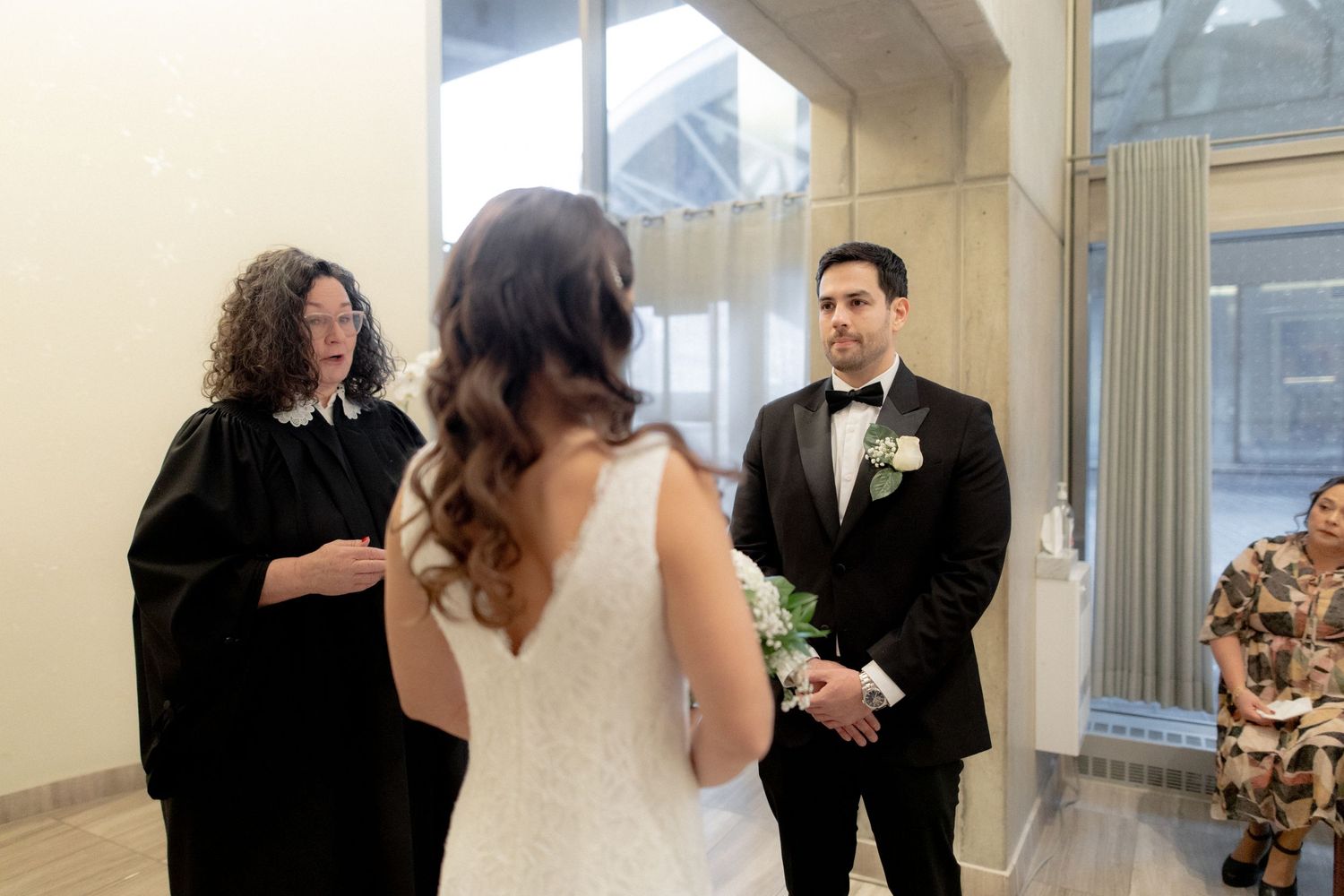 Wedding ceremony in progress in a bright, modern space with glass windows.