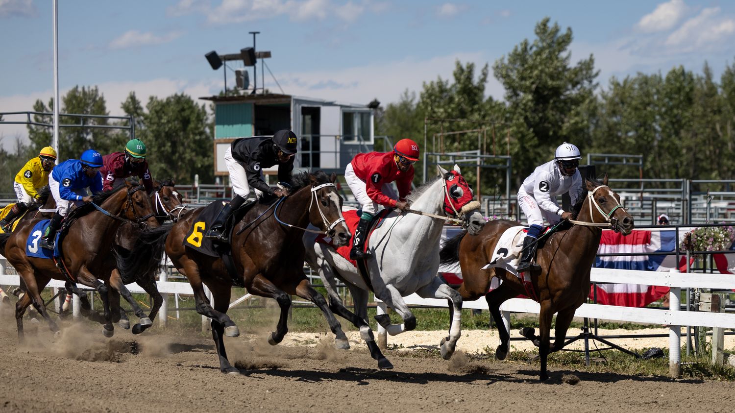Horses and jockeys racing on a dirt track during a competitive horse race.