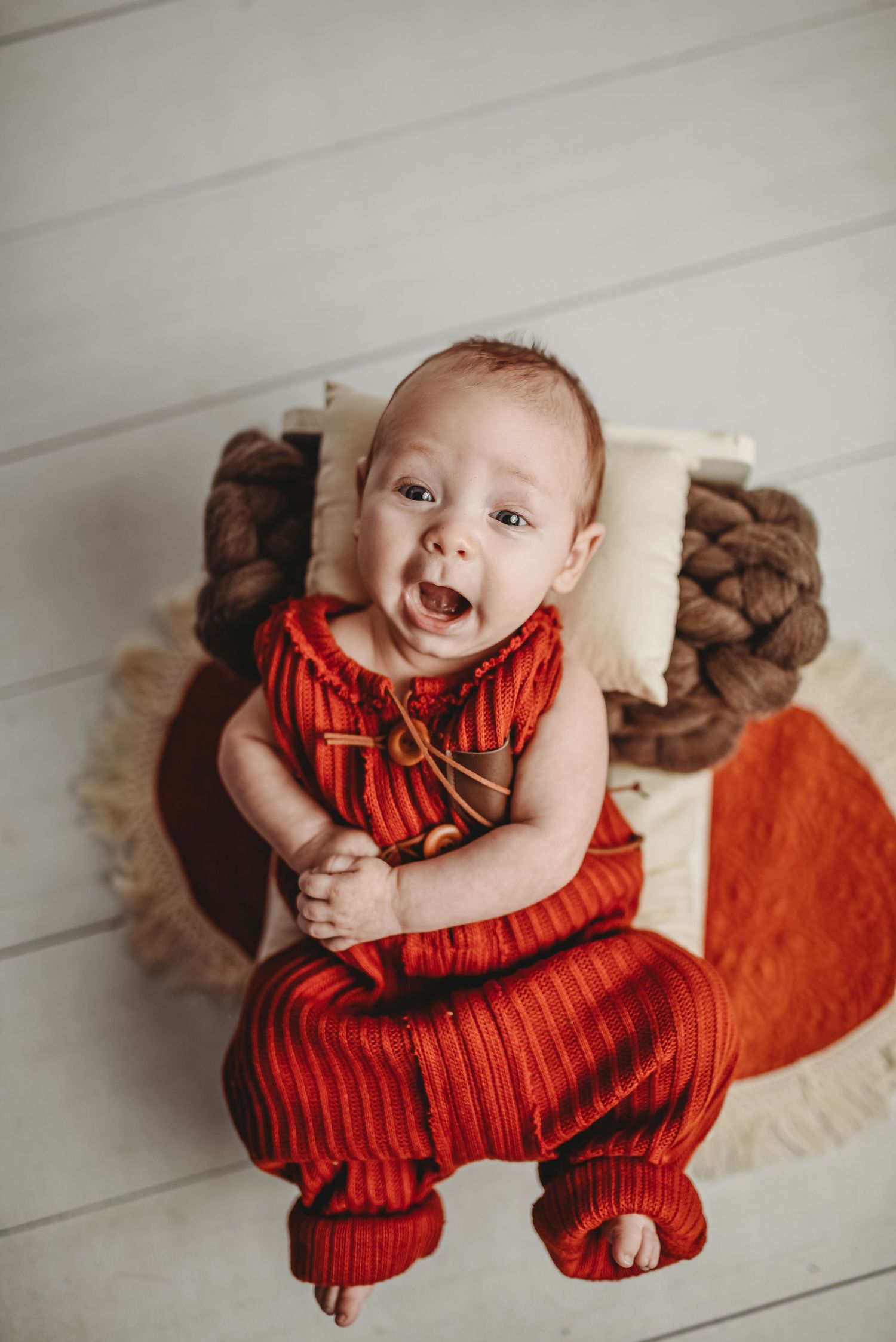 Baby wearing red striped romper lying on white floor with brown plush toys.
